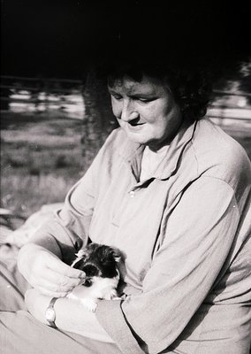 Black-and-white portrait of an elderly woman cradling a small, white-and-brown dog, likely a terrier. She wears a collared bl...