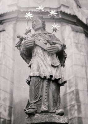 Relief sculpture of robed figure holding a staff topped with three stars and a book. Likely a saint or religious icon, possib...
