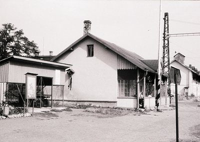 Single-story rural station building with gabled roof, corrugated metal siding, and a chimney, flanked by utility poles and a ...