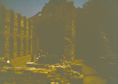 Vintage sepia-toned photograph of ancient stone ruins with weathered columns and arched doorways, likely from a Southeast Asi...