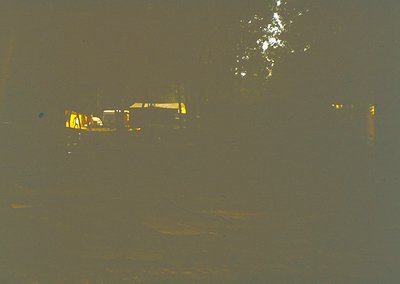 Vintage sepia-toned photo of a dimly lit industrial scene, featuring a single-story brick building with yellow-painted window...