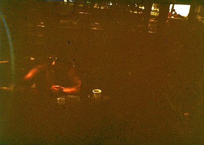 Vintage low-angle shot of a person reclining on a sandy beach, silhouette framed by warm amber tones. Empty glass and cigaret...