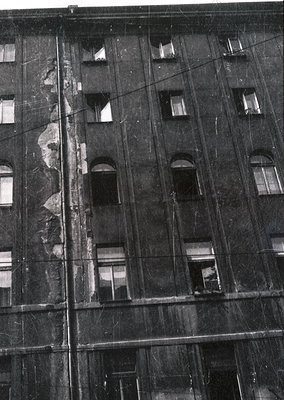 Mid-century urban architecture featuring a multi-story brick facade with arched window frames. Visible wear and exposed wirin...