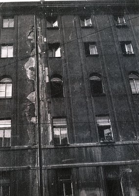 Mid-century Soviet-era concrete apartment block façade, showing structural damage and exposed rebar. Symmetrical arched windo...