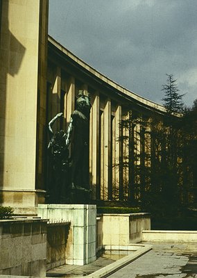 Neoclassical building façade featuring a dynamic bronze statue of a man in mid-leap, set against tall columns and stone steps...
