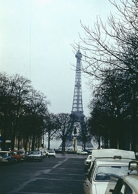 Classic Eiffel Tower framed by bare winter trees, Paris . Narrow street lined with vintage cars and parked vehicles, evoking ...