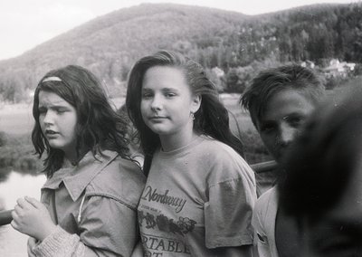 Black-and-white portrait of three young women in outdoor setting, likely 1970s. Center figure wears a "Nordway Portable" t-sh...