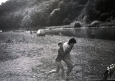 Mid-20th century black-and-white photo of two children playing near a rocky hillside. Blurred motion captures dynamic energy....
