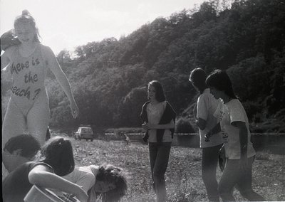 Black-and-white protest scene: A large inflatable cutout of a person holding a sign reading *"Where is the beach?"* draws att...