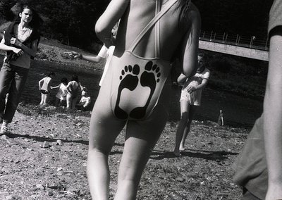 Black-and-white photo capturing 1970s beachgoers in swimwear with playful paw-print designs. Group of people lounging on rock...
