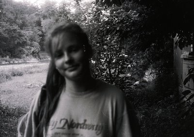 Vintage black-and-white portrait of a smiling individual in a "Nordberg" t-shirt, blurred background with foliage and partial...