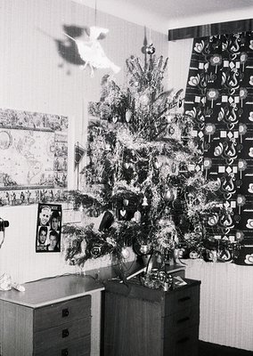 Vintage black-and-white interior featuring a densely adorned Christmas tree with tinsel, geometric ornaments, and a star topp...