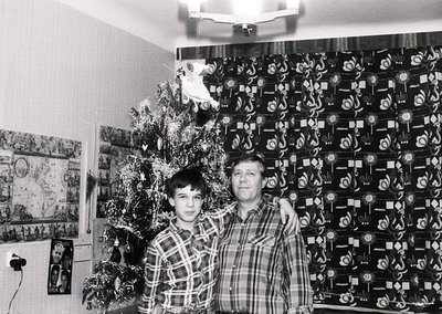 Black-and-white indoor portrait of a man and boy posing beside a decorated Christmas tree and wall adorned with geometric wal...