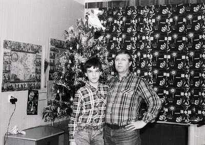A black-and-white portrait of a man and boy in a Soviet-era home, likely 1970s–1980s. The man wears a plaid shirt, the boy a ...