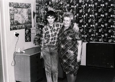 A black-and-white family portrait from the 1970s–1980s, featuring a young man and woman in patterned clothing standing indoor...