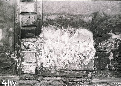 War-damaged building facade with exposed brickwork and plaster collapse, likely post-WWII. Distinctive vertical stone columns...