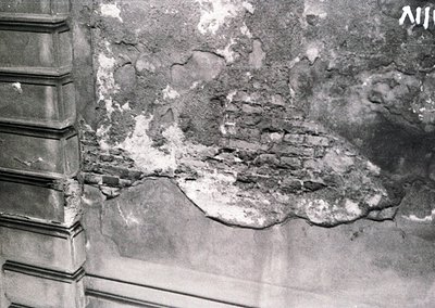 Close-up of deteriorated plaster revealing exposed brickwork, likely from a historic European building. Cracks and peeling su...