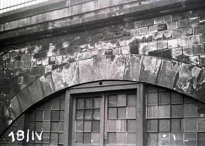Architectural detail of a brick archway with weathered stonework and double-pane windows, likely industrial or institutional....