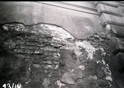 Close-up of deteriorated plaster and exposed brickwork, likely from a historic building’s interior. Cracks and crumbling reve...