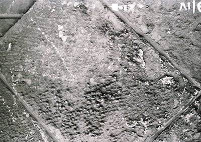 Close-up of weathered concrete surface with visible cracks, erosion, and embedded debris, likely from mid-20th century constr...