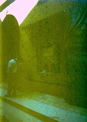 Reflection of a lone figure in a yellow-tinted glass wall, likely a modern office or institutional building. The person appea...