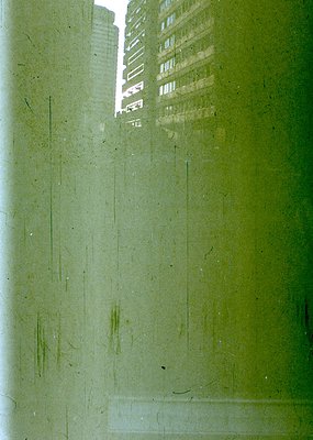 Reflection of high-rise buildings through a slightly fogged or scratched glass pane, likely a window. Urban architecture with...