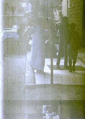 Double-exposure urban reflection on glass, blending two distinct scenes: a shadowy figure ascending stairs and a blurred, lig...