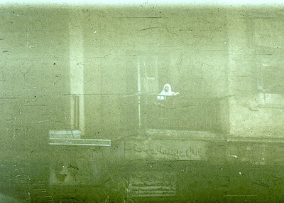 Vintage train window view showing blurred interior with faint graffiti: "Farewell" and a small figure seated. Likely mid-20th...