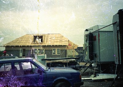 Vintage photo of a partially constructed house with exposed wooden framing and brickwork, likely mid-construction in the 1970...