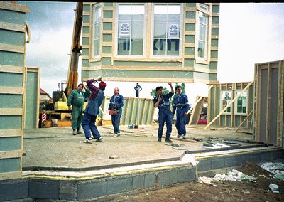 Construction crew collaboratively lifts prefab concrete beams at mid-rise building site, featuring Soviet-era architectural s...