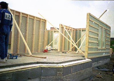 Construction frame under assembly with wooden beams and glass panels, likely mid-1980s–1990s. Worker in blue uniform (possibl...