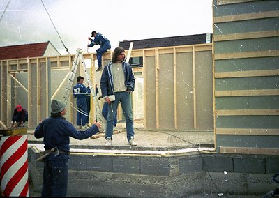 Construction crew erects prefab panel walls, 1970s-80s Eastern Bloc style. Workers in matching blue overalls and hard hats as...