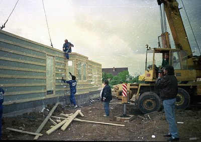 Construction crew assembling prefab concrete panels on-site, with crane assistance. Workers in blue uniforms and hard hats se...