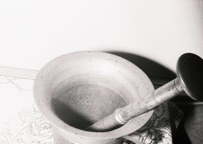 Vintage mortar and pestle in use, likely for grinding herbs or spices. The wooden pestle shows wear, suggesting frequent use....