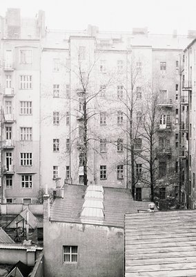 Mid-century urban courtyard with Soviet-era apartment blocks, featuring symmetrical window alignments and flat roofs. Bare wi...