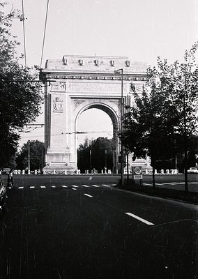 Neoclassical triumphal arch with intricate carvings and decorative columns, flanked by trees and street lamps. Likely a histo...