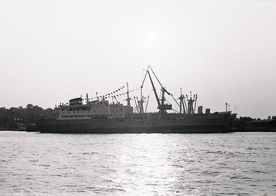 Mid-20th century cargo ship with cranes, likely a Soviet-era bulk carrier or ferry, sailing on calm waters. Decorative flags ...
