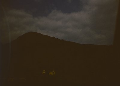Vintage sepia-toned landscape featuring a lone, isolated house with a sloped roof under dramatic storm clouds. The scene evok...