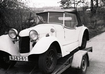 Vintage white convertible car (likely 1930s-1940s) on a trailer, featuring rounded fenders, dual headlamps, and a soft-top ro...