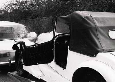 Vintage convertible with classic rounded fenders, whitewall tires, and a rolled-down leather roof, parked beside a utilitaria...