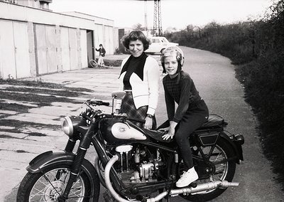 Vintage black-and-white photo of a woman and child seated on a classic motorcycle, likely a BSA or similar British model, in ...