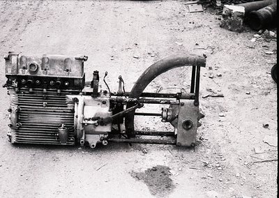 Vintage industrial engine with radiator fins, hand crank, and exposed mechanical components, likely mid-20th century. Rust an...
