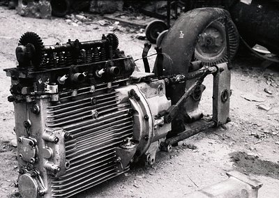 Vintage industrial engine with exposed cylinder fins, gearing, and flywheel, likely from mid-20th century machinery. Rust and...