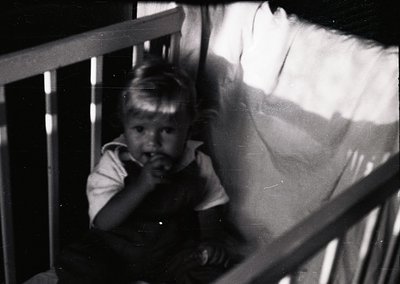 Young child in vintage striped shirt peering through metal balcony railing, mid-20th century. Soft focus and grainy texture s...