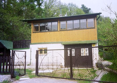 Mid-century modern wooden house with yellow upper floor and white lower level, featuring large windows and a gabled roof. Wro...