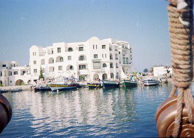 Mediterranean coastal architecture with curved balconies and whitewashed facades reflects in calm waters. Traditional fishing...