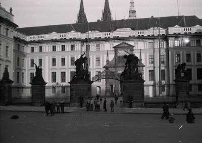 Black-and-white shot of Prague Castle’s **St. Vitus Cathedral spires** and **Old Royal Palace** façade, framed by ornate wrou...
