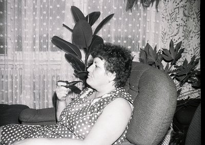Mid-20th century indoor portrait of a woman in a polka-dot dress, holding a cigarette holder. She lounges on a patterned sofa...