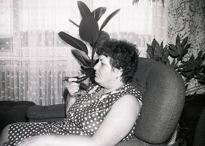 Mid-century indoor portrait of a woman in a polka-dot dress, holding a cigarette, seated on a tufted armchair beside a large ...