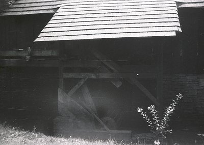 Mid-century modern garage with gabled, corrugated metal roof and exposed wooden beams. Brick foundation and partial view of a...